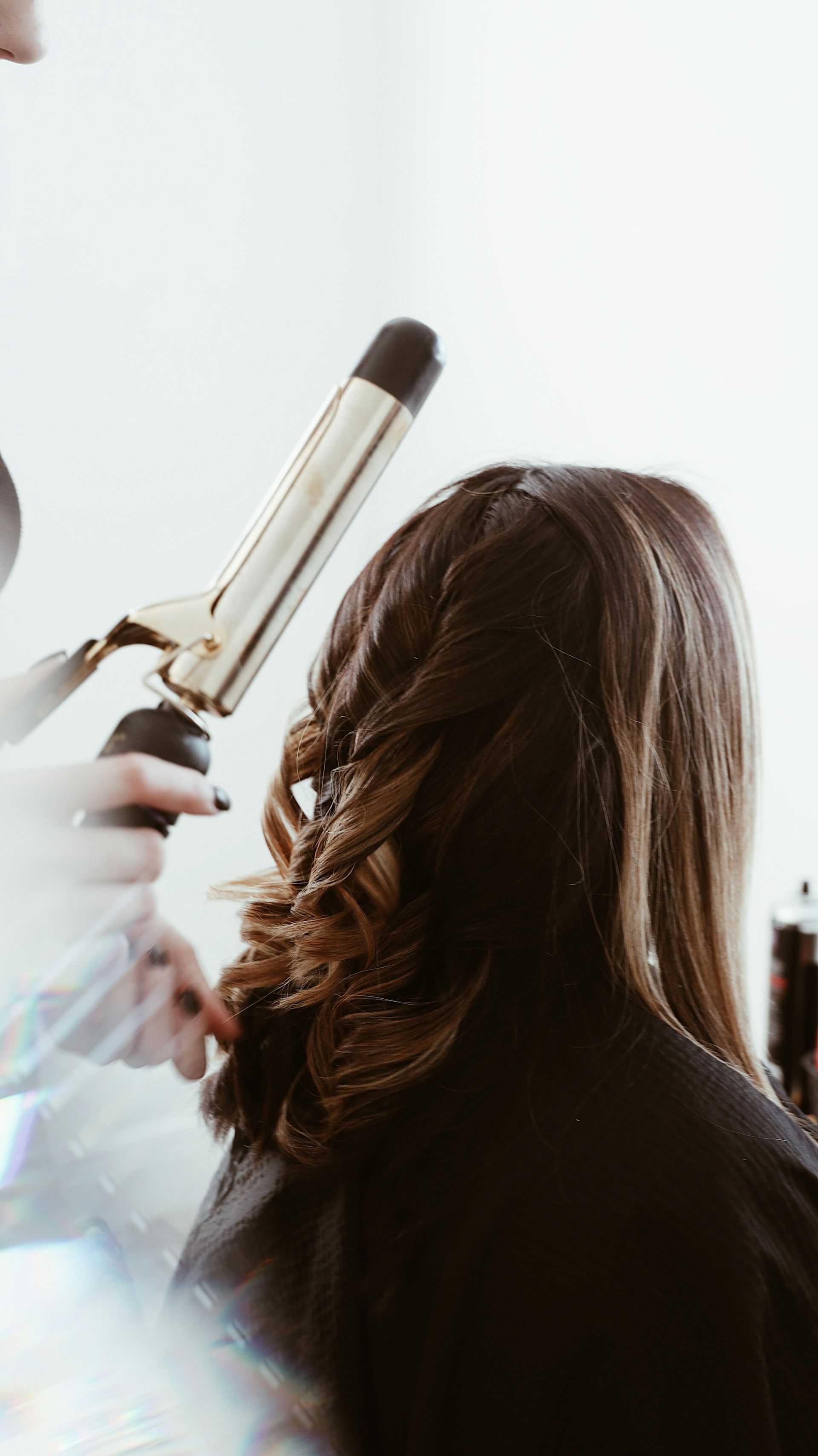 Hair stylist curling a woman's long brown hair with a curling iron.