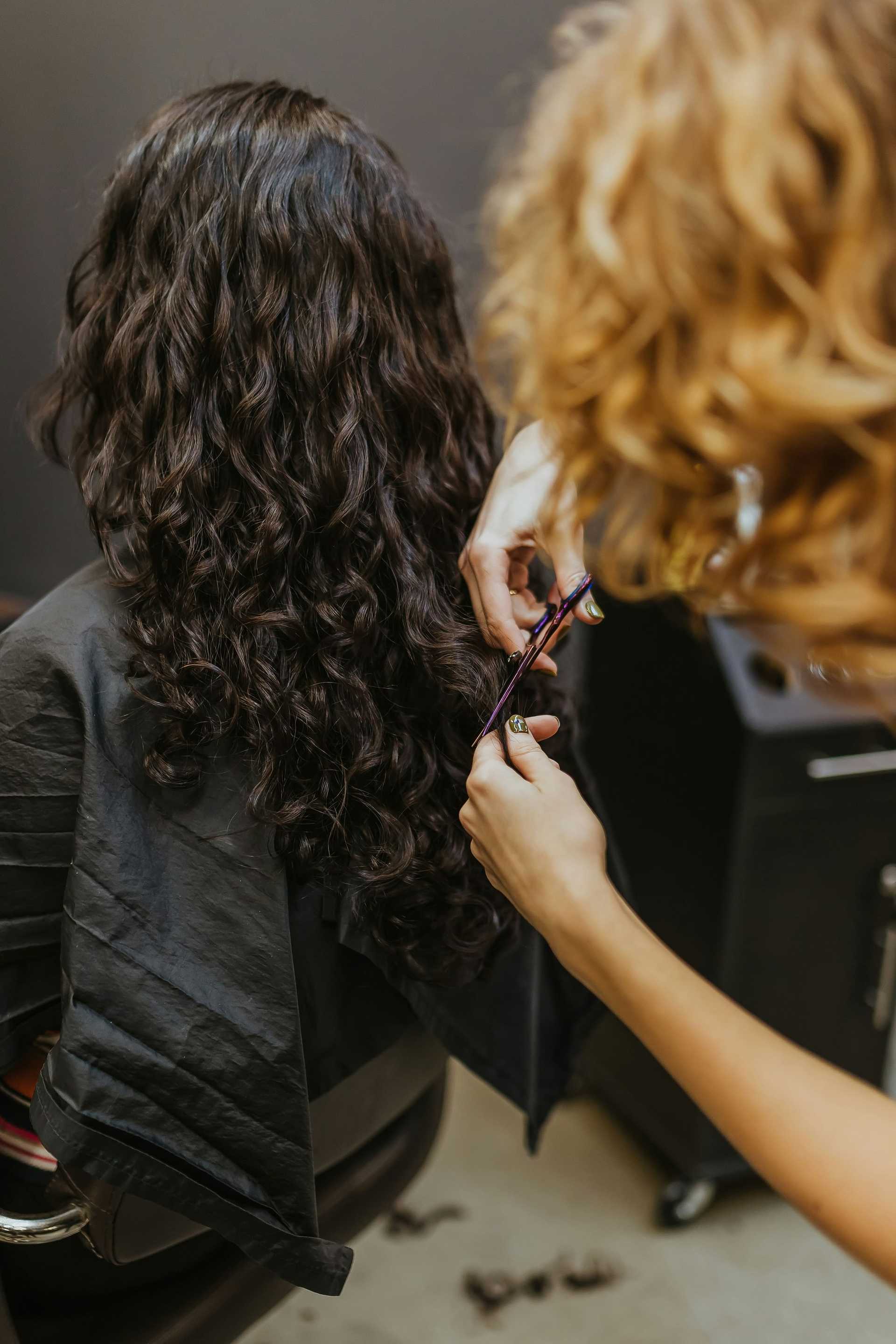 Hair stylist cutting long curly hair in a salon chair.